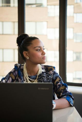 Businesswoman in stylish office attire working on laptop by window, conveying professionalism and focus.