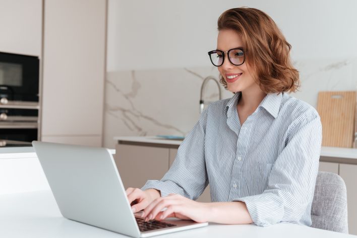 A businesswoman in a modern office intently working on a laptop and writing in a notebook.